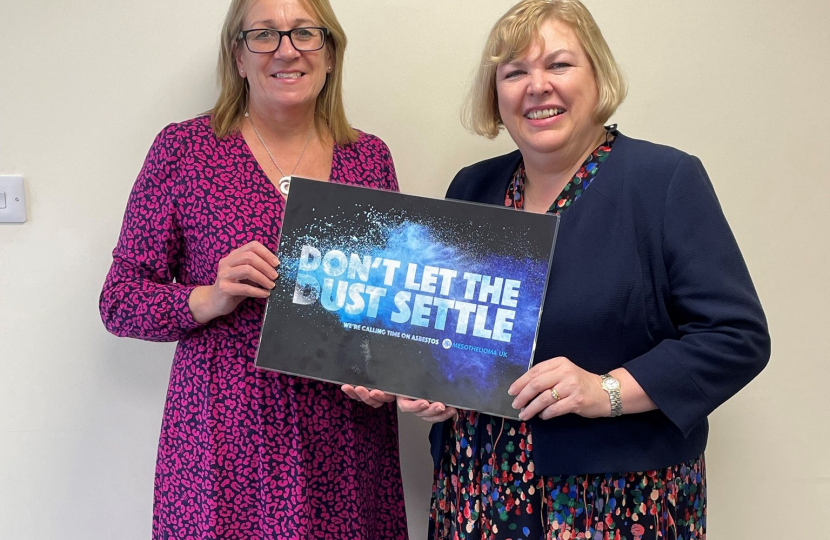 Jane with a representative from Mesothelioma UK holding a 'Don't let the Dust Settle' board